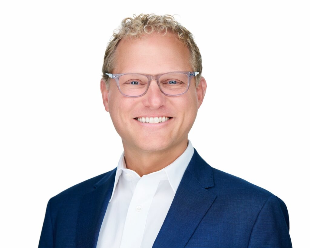 Andy Strunk headshot — White background, blue coat, smiling
